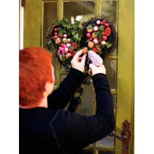 Donna che fissa decorazioni a una ghirlanda a forma di cuore con una pistola per colla a caldo. Pistola per colla a caldo dalla categoria.