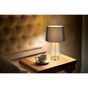 Elegante lampada da tavolo con paralume grigio e base in vetro trasparente su un comodino.