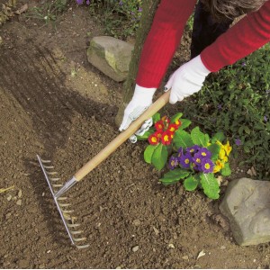 Persona che indossa guanti a maglia fine LUX taglia 9 rastrella in giardino.