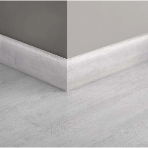 Battiscopa t.b.t. bianco su parete grigia e pavimento in legno chiaro.