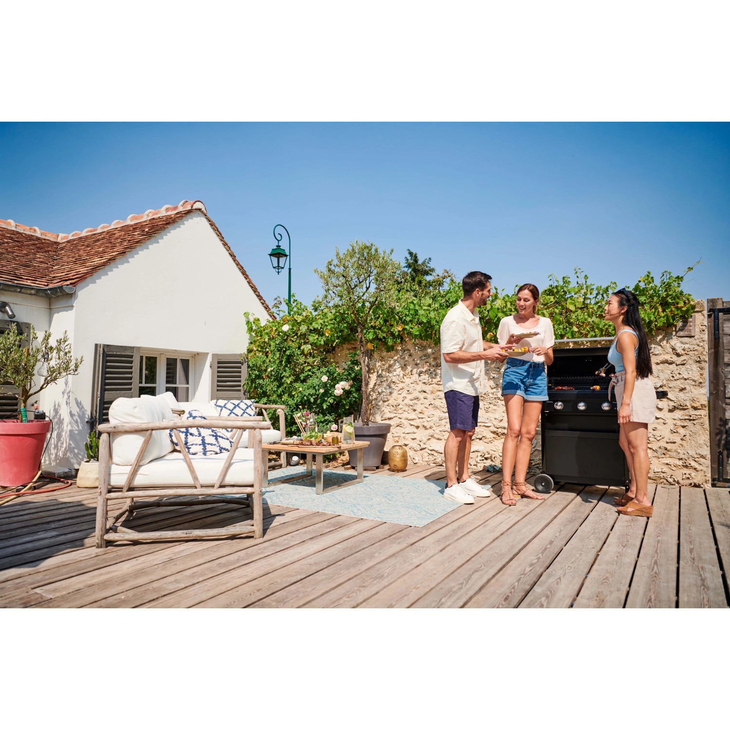 Scena con barbecue a gas t.b.t. in giardino con tre persone che grigliano.