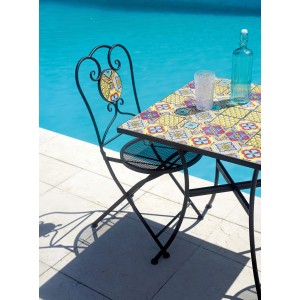 Tavolo da giardino con motivo a piastrelle e sedia con struttura in metallo a bordo piscina.