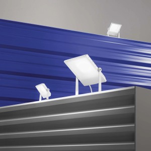 Diversi faretti da cantiere a LED t.b.t. bianchi su sfondo blu e grigio.