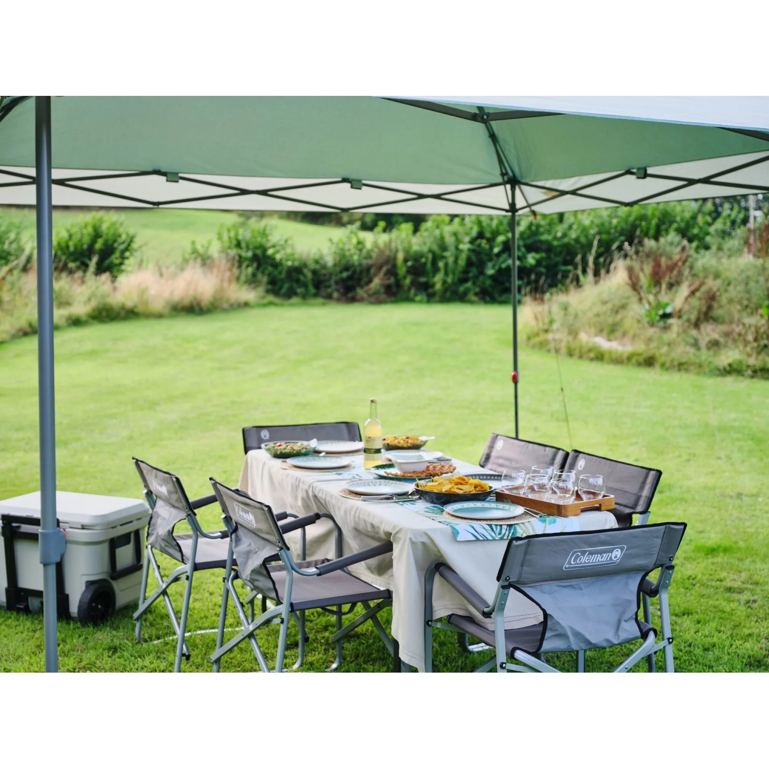 Coleman FastPitch Shelter L, verde e bianco, con tavolo e sedie in giardino.