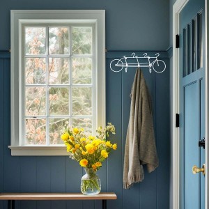 Appendiabiti da parete a forma di bicicletta con giacca e fiori in corridoio blu.