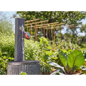 Computer per irrigazione su rubinetto con colonna in pietra e vasca di raccolta in giardino.