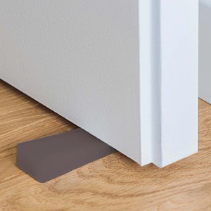 Fermaporta (Fermaporte) grigio e piatto sotto una porta bianca su pavimento in legno.