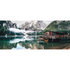 Paesaggio idilliaco con lago di montagna, montagne boscose e una piccola casa di legno sulla riva.