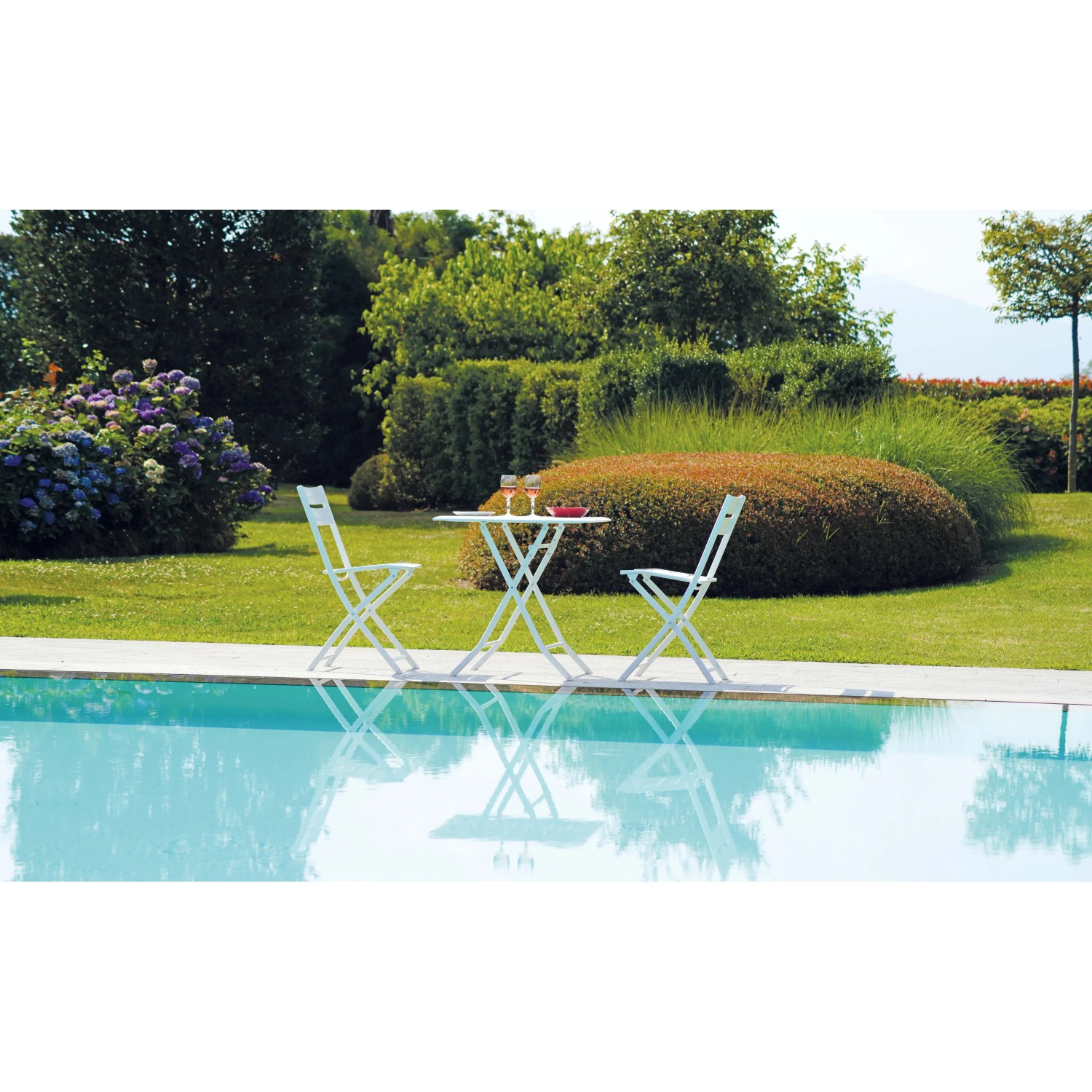Set di mobili da giardino bianchi a bordo piscina: tavolo e due sedie. Ideale per rilassarsi all'aperto.