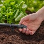 Primo piano di una mano che installa un sistema di microirrigazione t.b.t. in giardino.