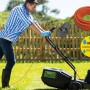 Uomo che taglia l'erba con tosaerba elettrico, cavo di prolunga e avvolgicavo in primo piano.