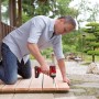 Uomo che utilizza l'avvitatore a impulsi a batteria Einhell TE-CI 18/1 Li Solo rosso su patio in legno.