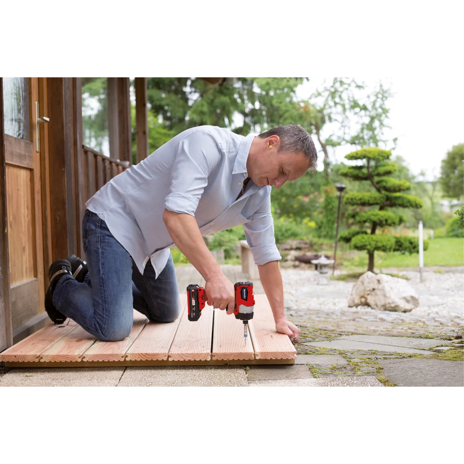 Uomo che utilizza l'avvitatore a impulsi a batteria Einhell TE-CI 18/1 Li Solo rosso su patio in legno.