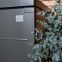 Dettaglio della Biohort StyleBox 170 box universale grigio scuro metallizzato, con logo, su parete in legno e pianta.