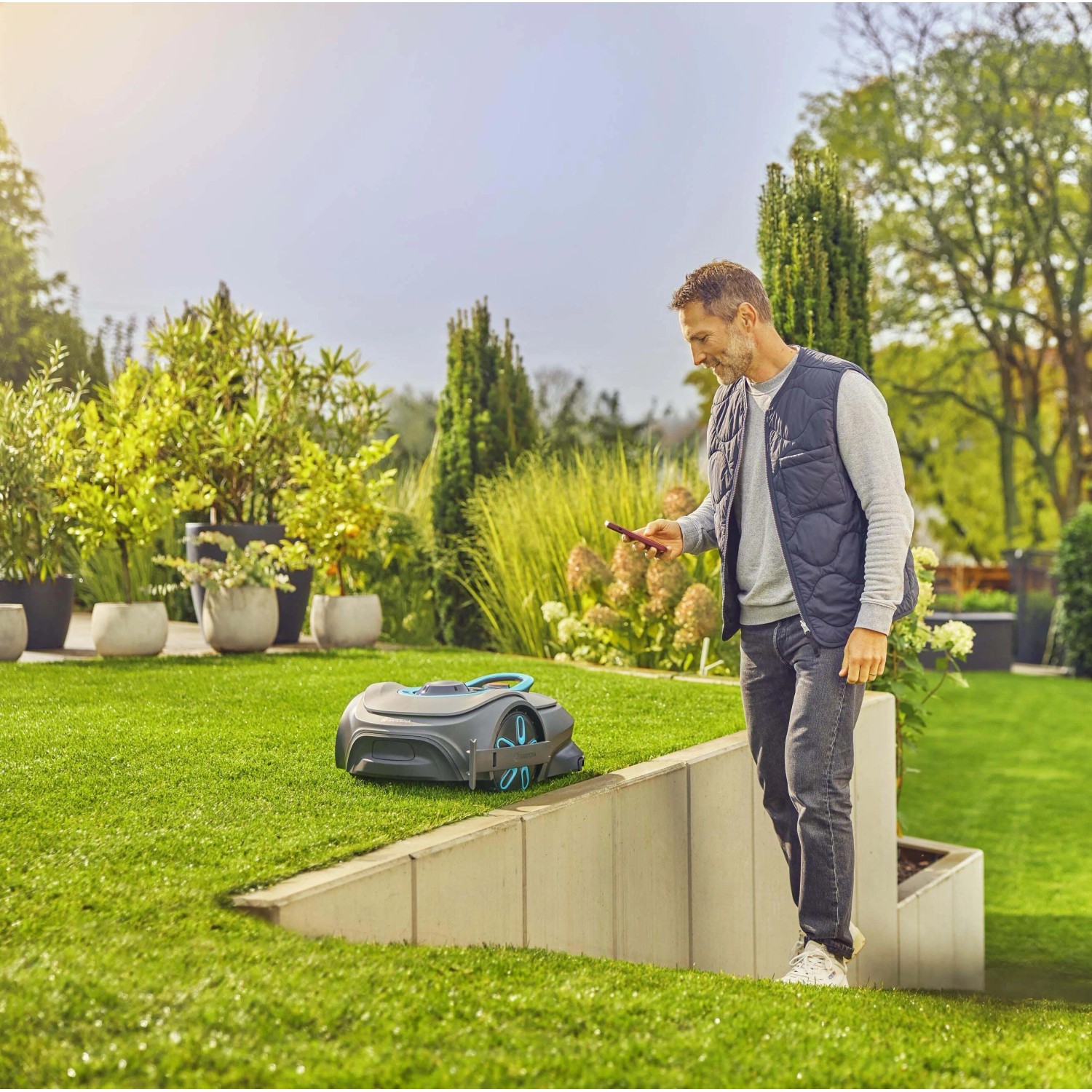 Uomo che utilizza robot tagliaerba in giardino tramite smartphone.