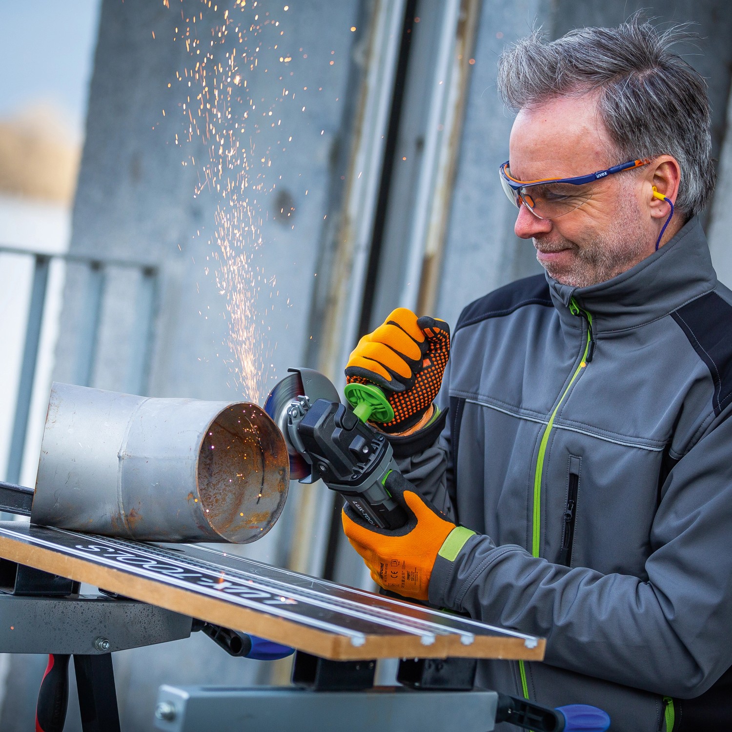 Uomo che smeriglia tubo di metallo con smerigliatrice angolare a batteria LUX A-WS-20/115. Scintille.