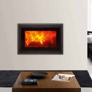 Stufa a legna t.b.t. con fuoco, incassata in una parete bianca.