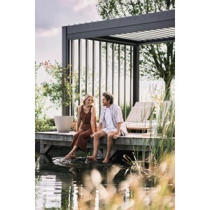 Pannello laterale a lamelle Biohort in grigio scuro metallizzato su pergola con coppia vicino all'acqua.