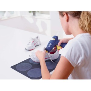 Donna usa pistola per colla a caldo blu t.b.t. su scarpa da ginnastica bianca.
