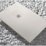 Piatto doccia rettangolare chiaro con scarico quadrato su ciottoli bianchi.