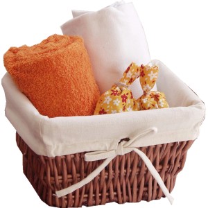 Cesto con accessori bagno: asciugamano arancione, panno bianco e sacchetti profumati.