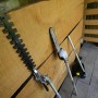 Diversi accessori per potatore e tagliasiepi t.b.t. appoggiati a una parete di legno.