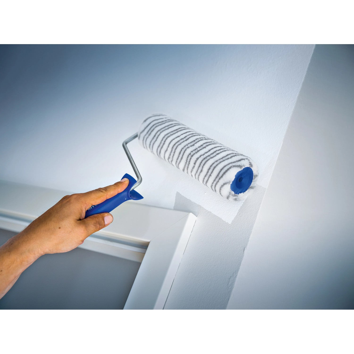 Rullo a dispersione LUX 25cm in azione: rullo per pittura a pelo corto a righe grigie che dipinge una parete.