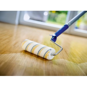 Rullo per vernice LUX PRO (blu-giallo, 18 cm) mentre vernicia un pavimento in legno.