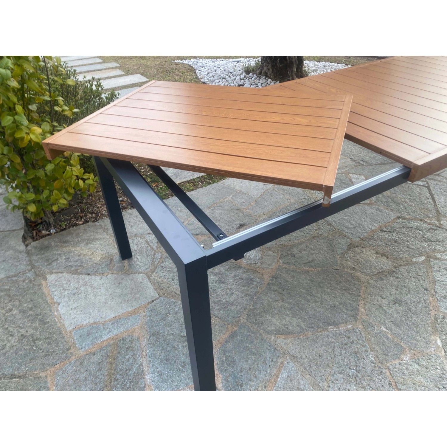 Tavolo da giardino allungabile con piano effetto legno e struttura in metallo grigio.