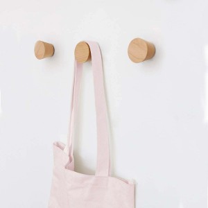 Tre appendiabiti rotondi in legno chiaro su una parete bianca, uno con una borsa di stoffa rosa.