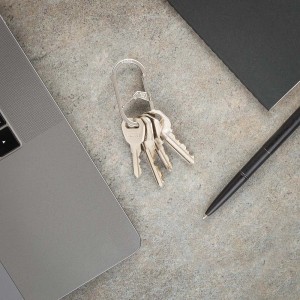 Portachiavi con diverse chiavi accanto a laptop e penna su un tavolo.