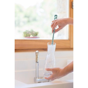 Donna pulisce caraffa di vetro con spazzola verde nel lavandino. Utensile da cucina per la pulizia.