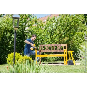 Uomo che vernicia una panca di legno con il sistema di verniciatura a spruzzo Wagner W950 Flexio in giardino.
