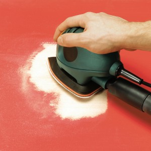 Levigatrice a mouse Black+Decker con set di tamponi abrasivi LUX in uso su superficie rossa.