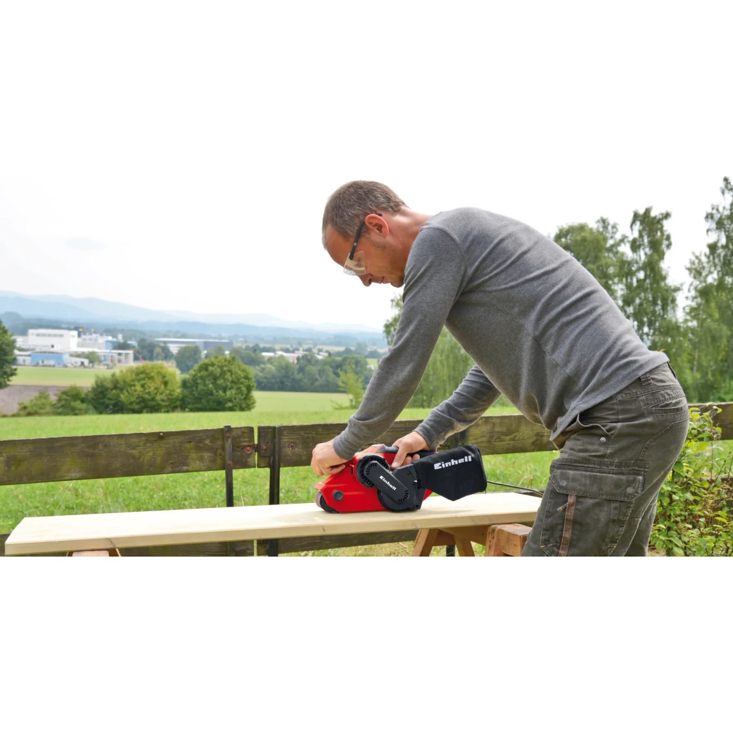 Levigatrice a nastro Einhell TC-BS 8038 in uso per levigare il legno. Levigatrice rossa con aspirazione polvere.