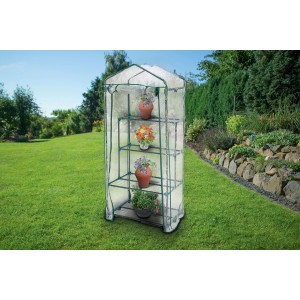 Piccola serra con ripiani e piante in giardino.