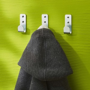 Tre ganci argentati su parete verde, uno con giacca. Ideale per pannelli forati.