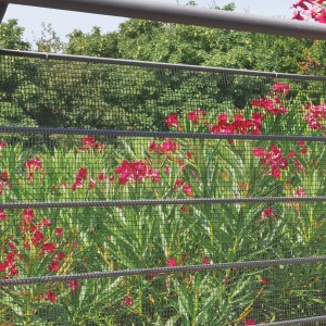 Fine rete metallica nera t.b.t. davanti a piante fiorite in giardino.