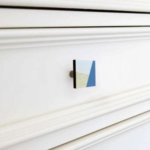 Pomello per mobili quadrato con motivo blu e beige su comò bianco.