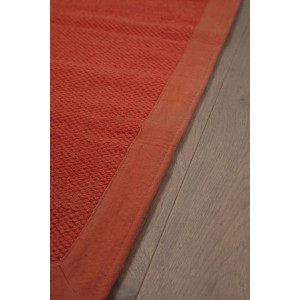 Dettaglio di una stuoia t.b.t. arancione con texture e bordo su pavimento in legno.