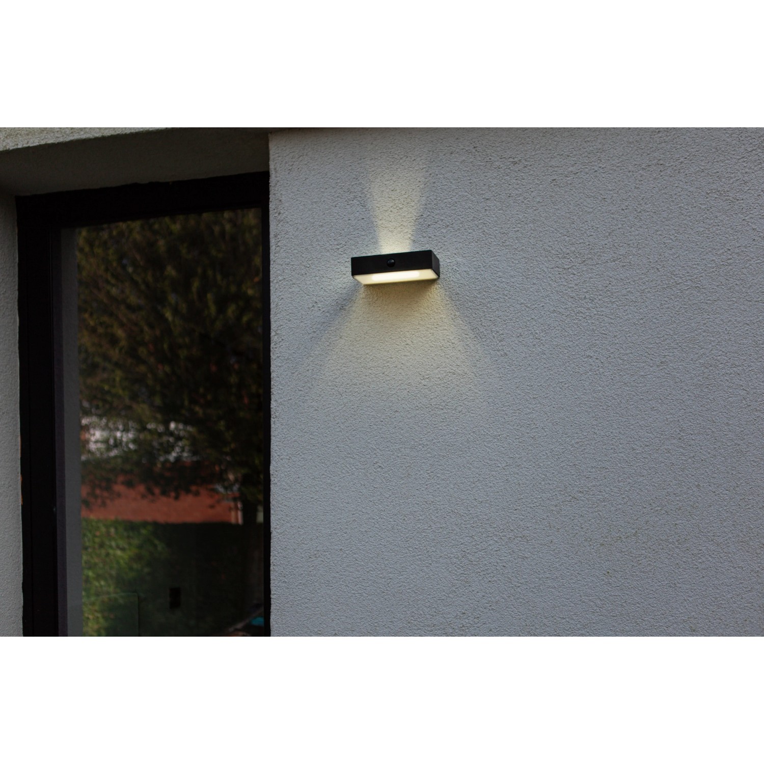 Lampada da parete solare a LED Lutec Fadi nera con sensore di movimento su muro grigio.