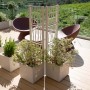 Fioriere quadrate bianche con supporto per piante rampicanti su una terrazza con vista.