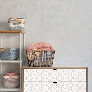 Pellicola decorativa con motivo astratto su cassettiera, cesti con biancheria sullo sfondo.