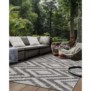 Tappeto da esterno grigio e bianco con motivo geometrico su un patio con mobili da giardino.