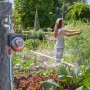 Timer per irrigazione Gardena su rubinetto in giardino, donna annaffia le piante.