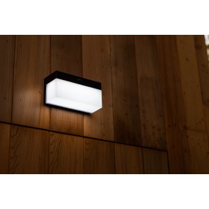 Lampada da parete solare a LED Lutec Fran nera con sensore di movimento su parete in legno.