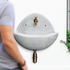 Fontana da giardino t.b.t. grigia con rubinetto in ottone su muro bianco.