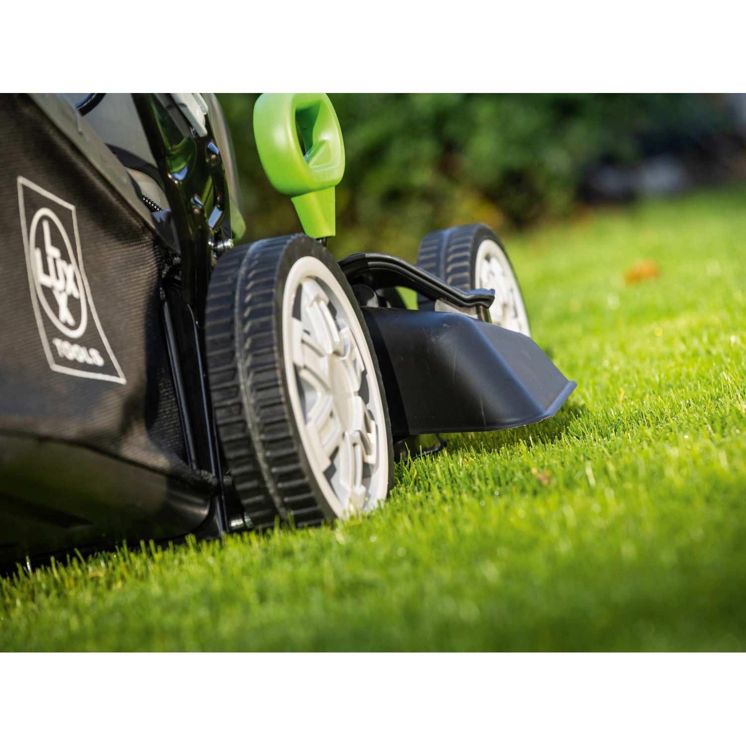 LUX-TOOLS Tagliaerba a batteria A-RM-46-24 in uso: Dettaglio delle ruote e del cesto di raccolta sull'erba.