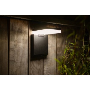 Lampada da parete solare a LED Lutec Moze nera e angolare con sensore di movimento su parete di legno.
