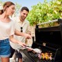 Coppia che griglia con barbecue a gas t.b.t. in giardino. Carne e verdure grigliate sulla griglia.